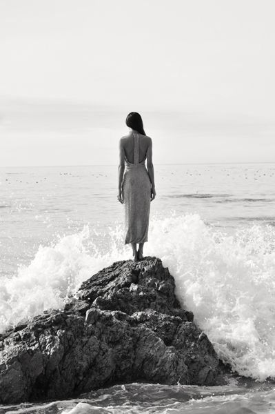 Woman in an evening dress standing on coastal rocks above the sea